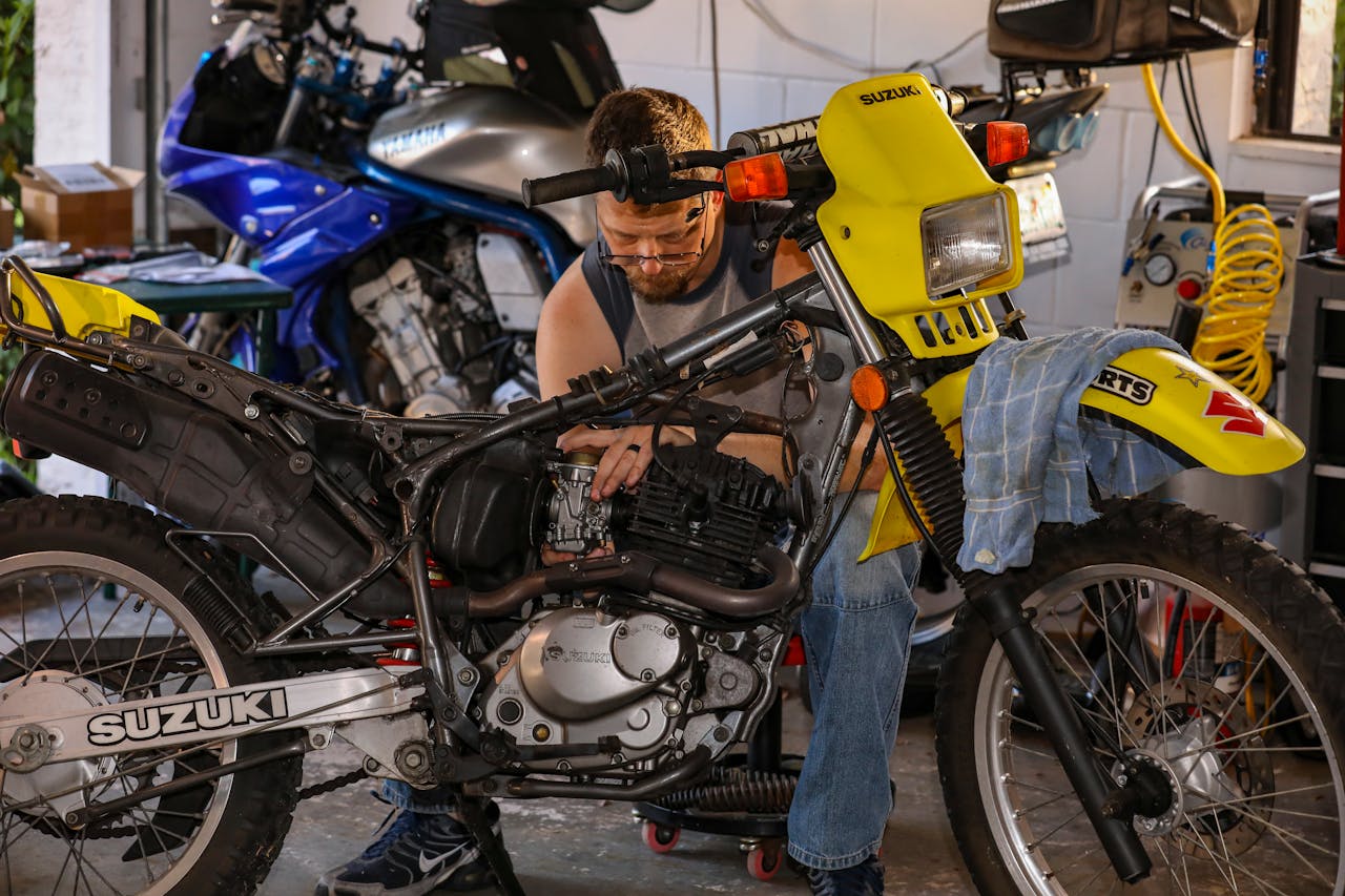 Mechanic repairing a Suzuki motorcycle in a cluttered garage, focusing on engine maintenance.
