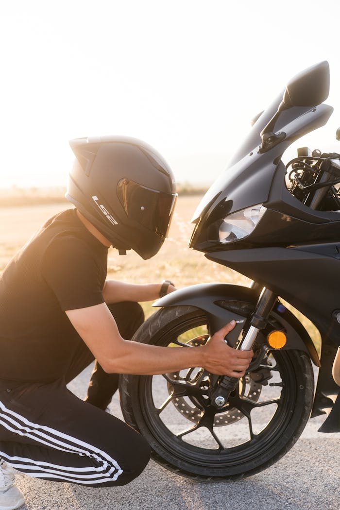 A person in a helmet examining a motorcycle tire during a sunny day outdoors.