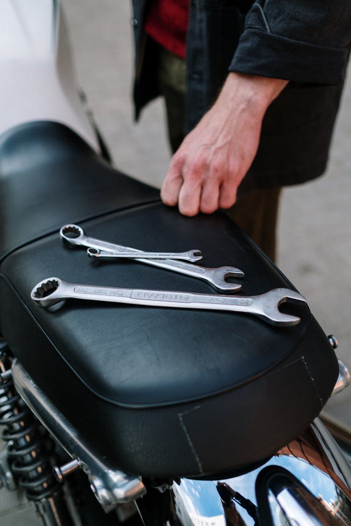 Close-up of mechanic's hand with tools on motorcycle seat.