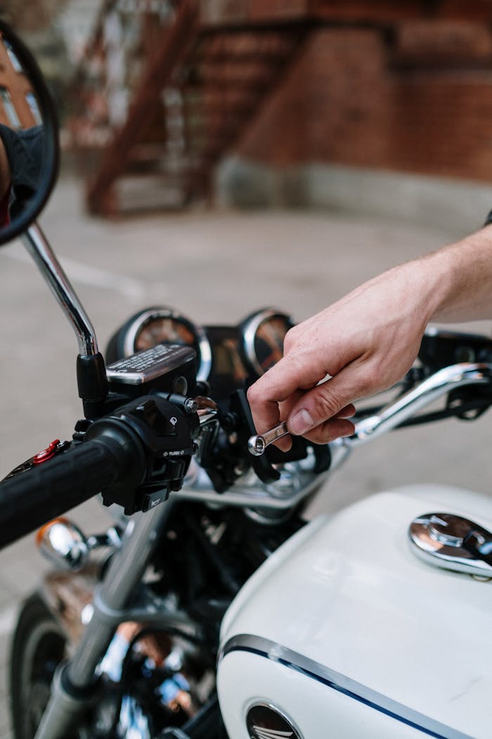 Detailed view of a hand using a wrench to tighten a motorcycle handlebar, highlighting maintenance work.